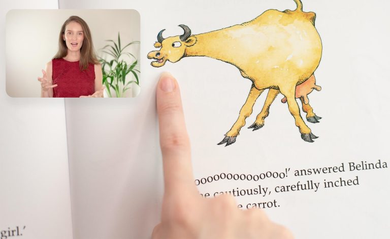 A person is pointing to an illustration of a cow in a book. An inset image shows a woman in a red top gesturing with her hands, possibly explaining or reading.