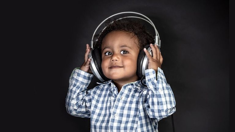 Child in a plaid shirt wearing large headphones, smiling against a dark background.