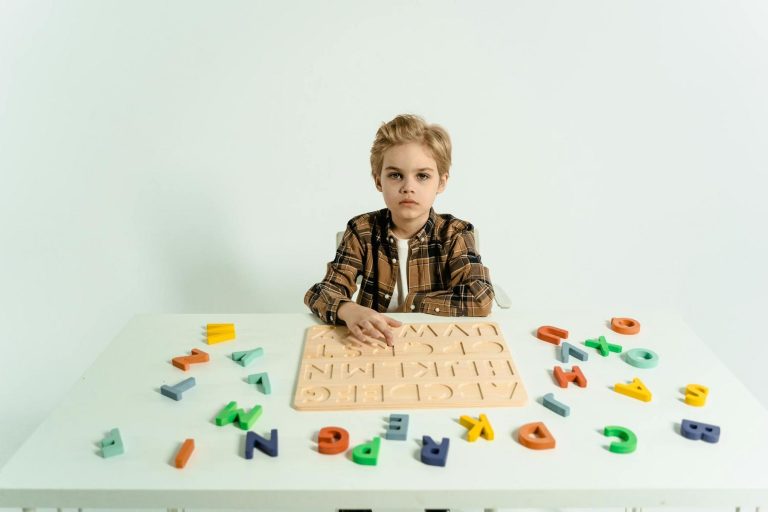 A child sits at a white table with scattered colorful alphabet letters and a wooden puzzle board.